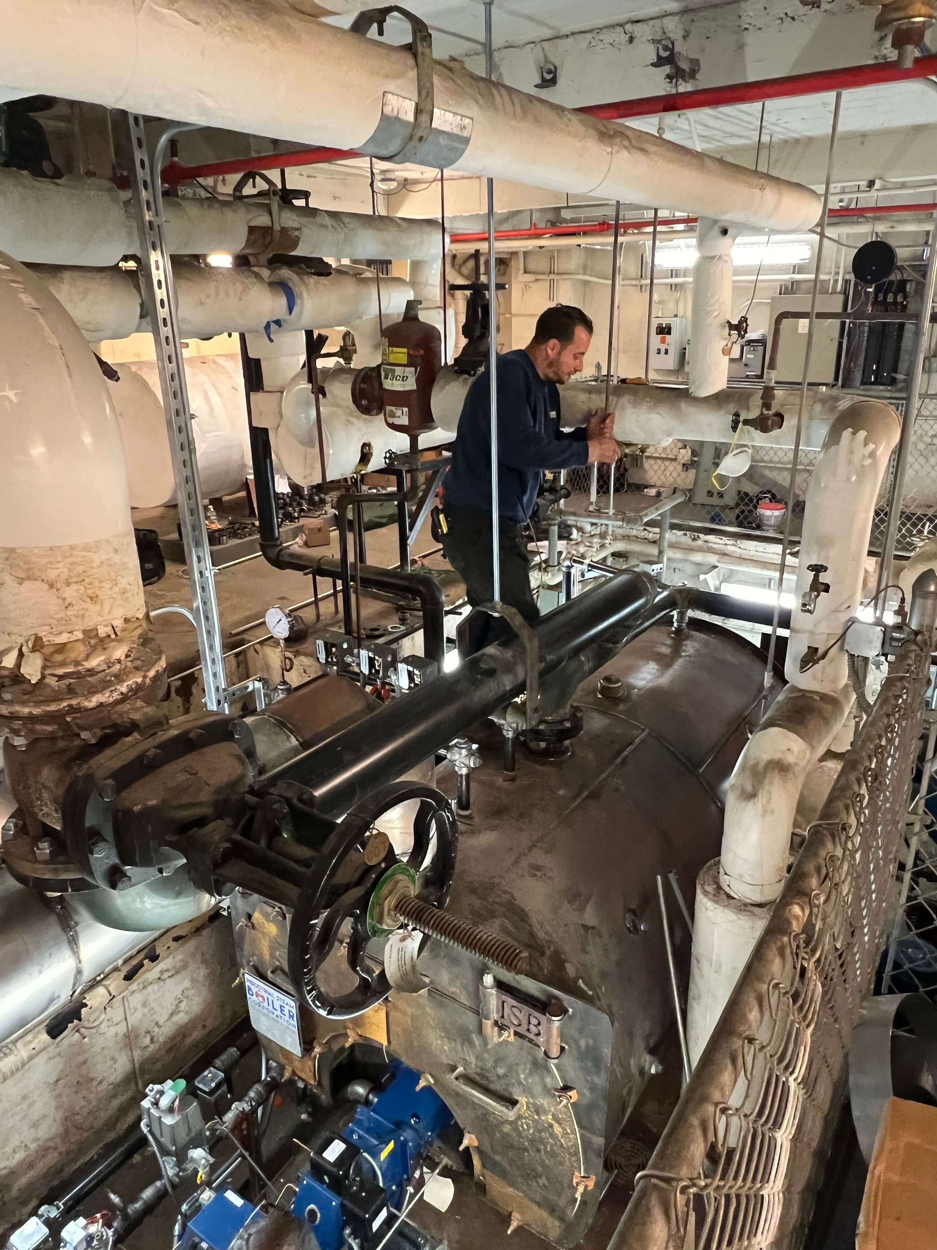 Man working on machinery in an industrial setting, with pipes and equipment visible.