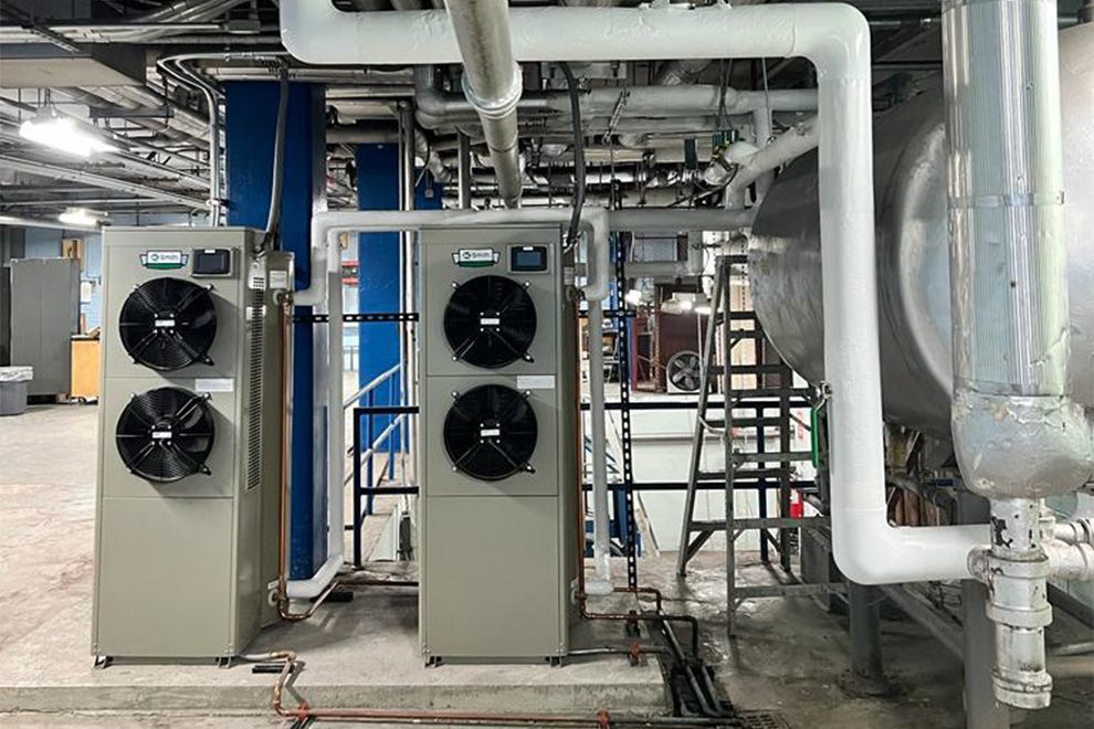 Industrial chillers with fans, pipes, and tanks in a mechanical room setting.
