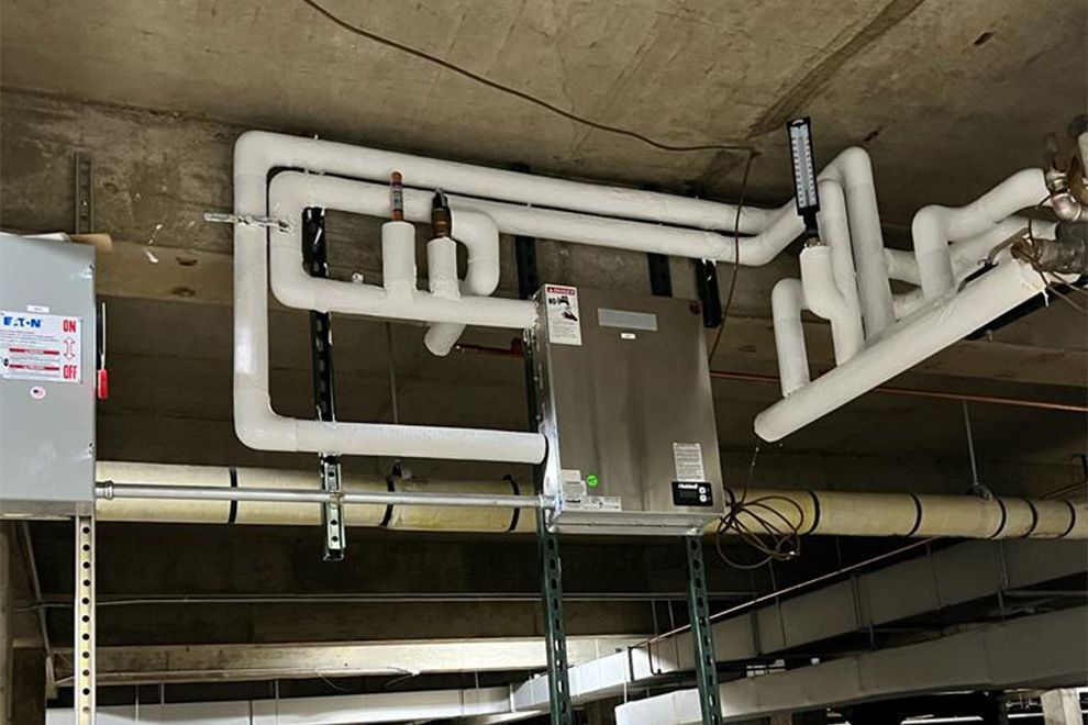 HVAC unit suspended from a concrete ceiling with insulated white pipes and electrical components.