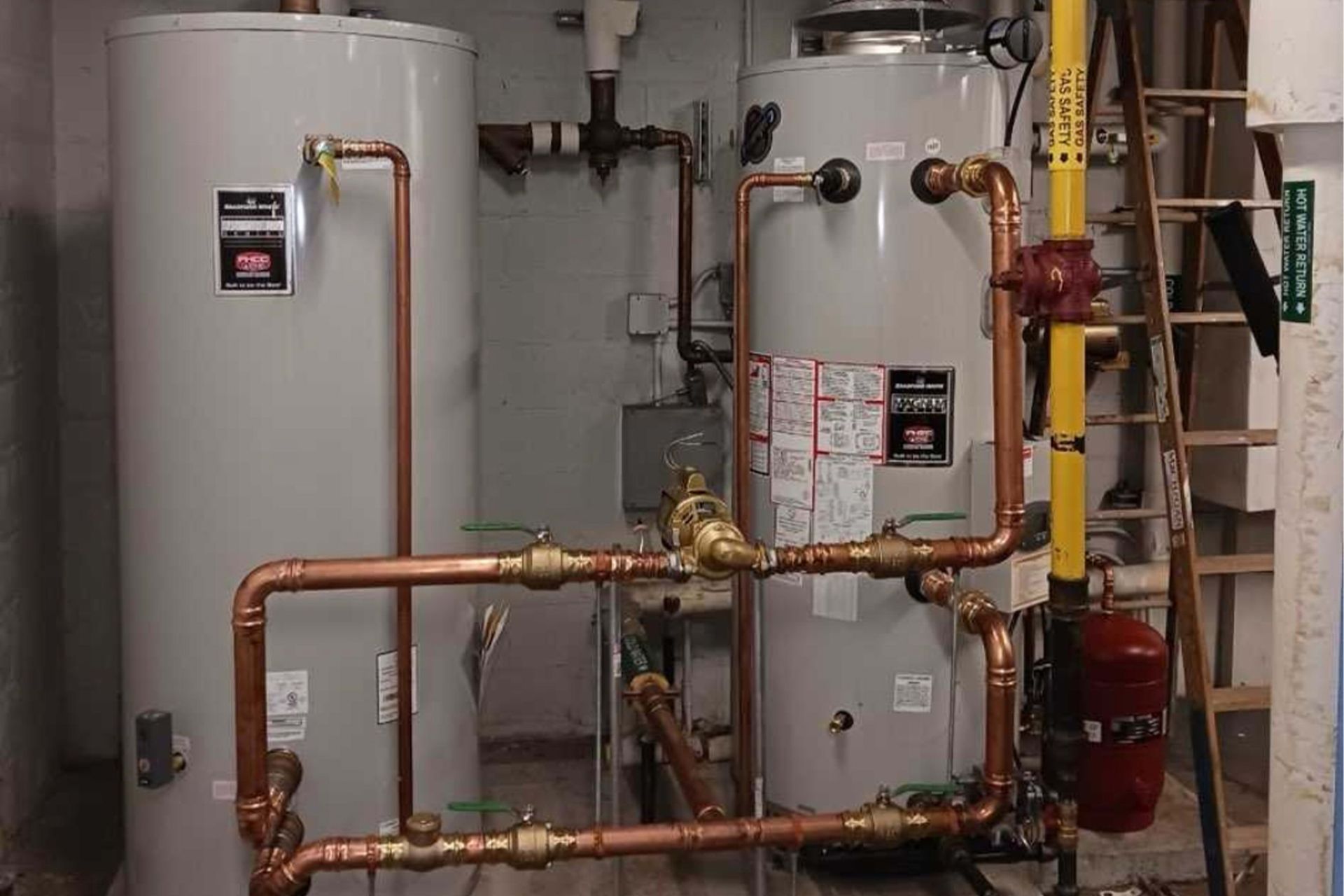 Two water heaters with copper pipes and valves in a utility room.