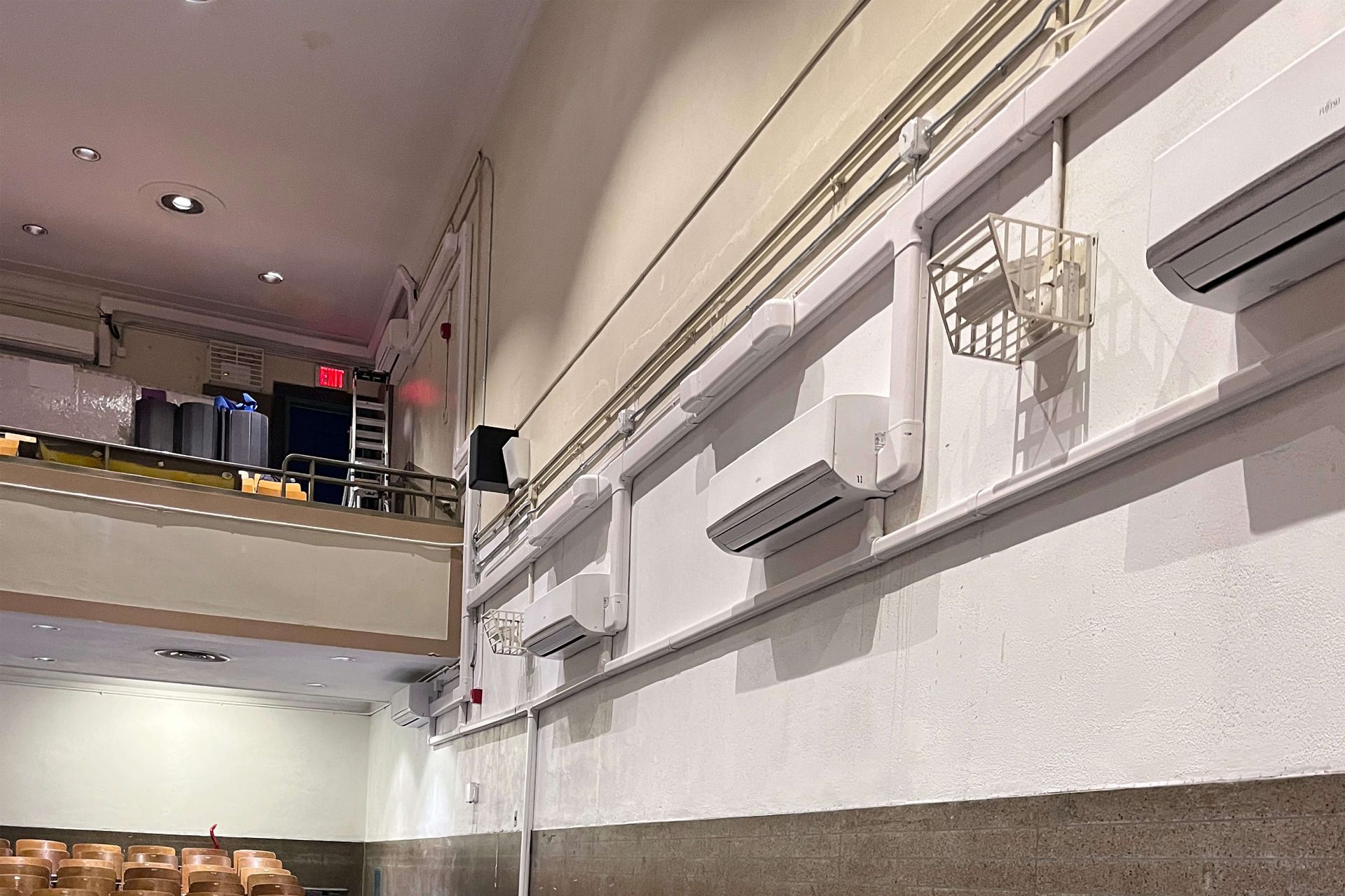 White interior wall with air conditioners and conduit running along it. A balcony with equipment is visible.