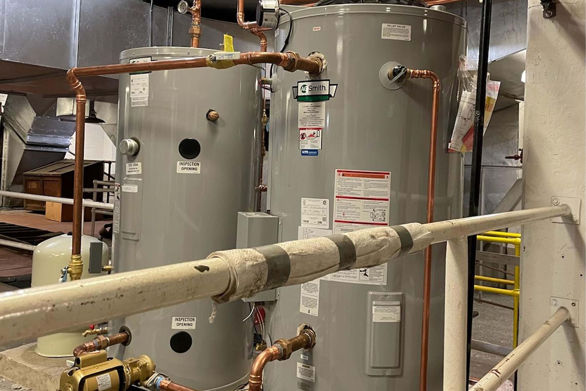 Two tall, gray water heaters with copper pipes in an industrial setting.