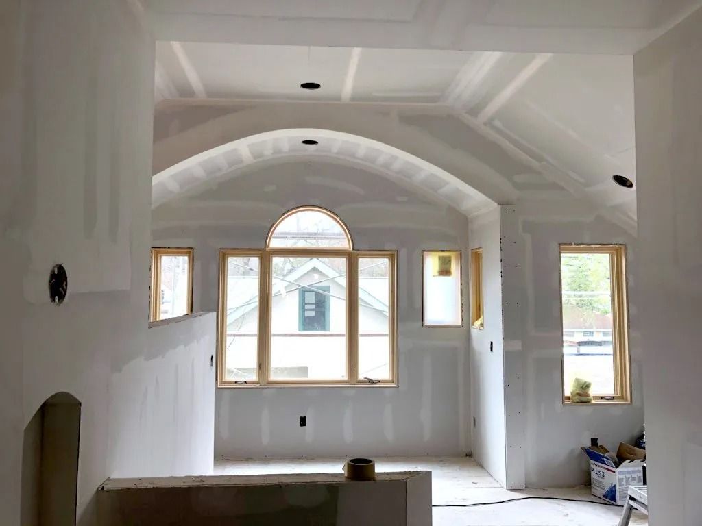 Interior of a room under construction with arched ceiling and windows. Drywall covers walls.