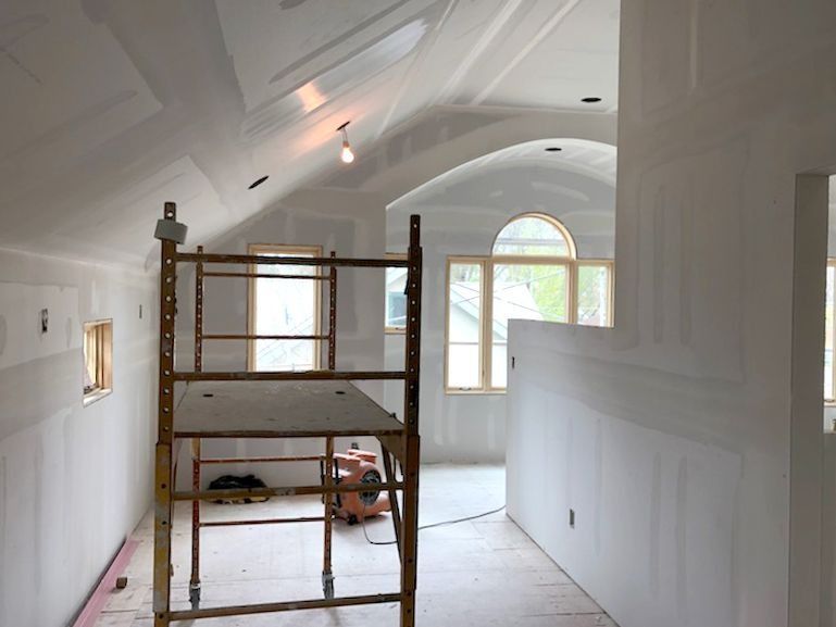 Interior room under construction with drywall, scaffolding, and windows.