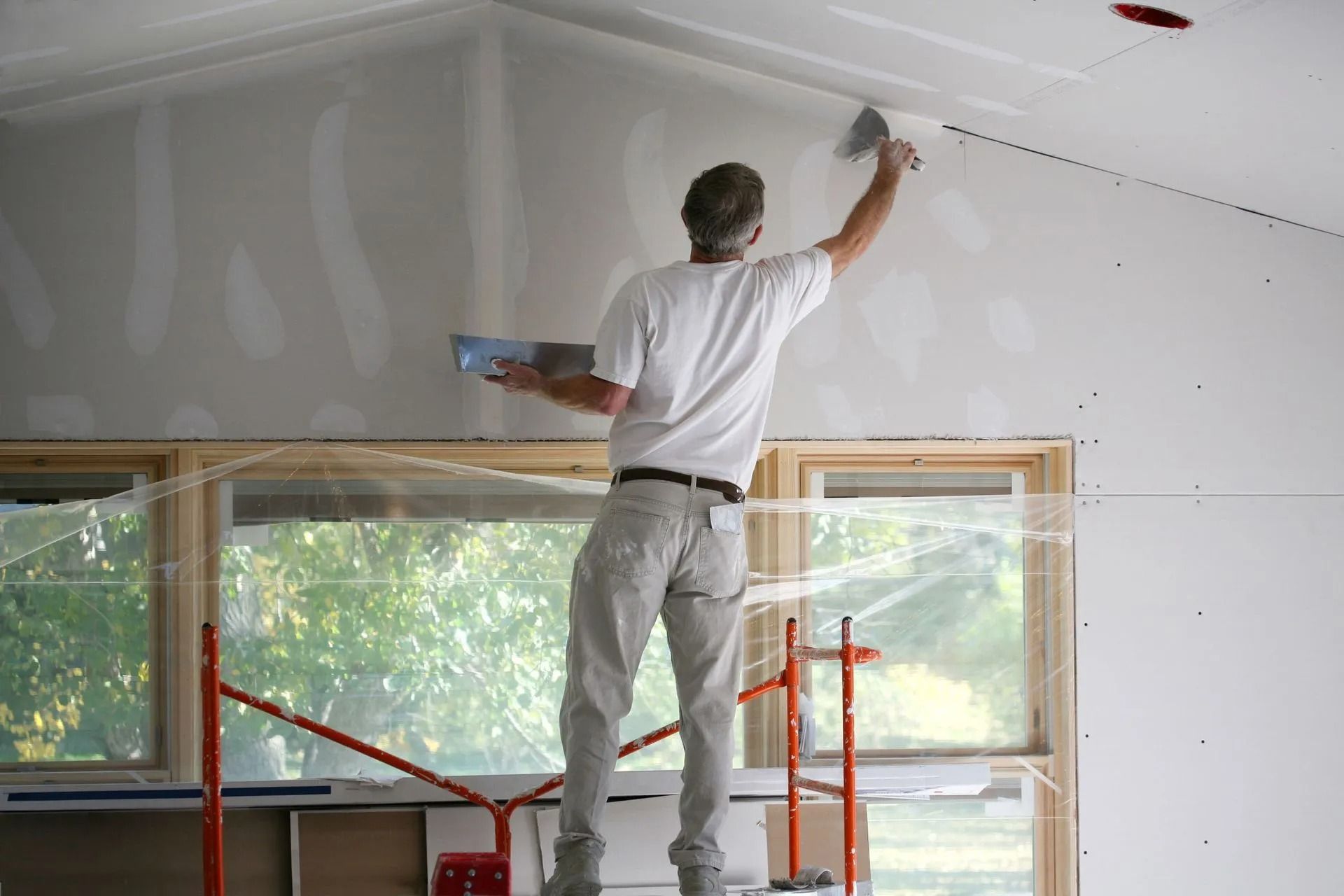 Person on scaffolding applying drywall compound to a ceiling.