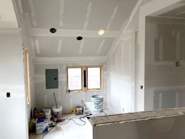 Interior room under construction with drywall installed on walls and ceiling; electrical work visible.