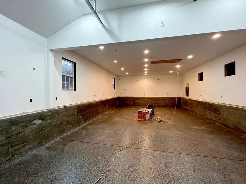 Interior of a garage with a newly poured concrete floor, partially finished walls, and overhead lighting.
