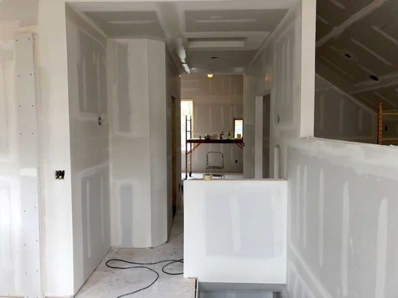 Interior hallway under construction; drywall installation, unfinished walls, white.