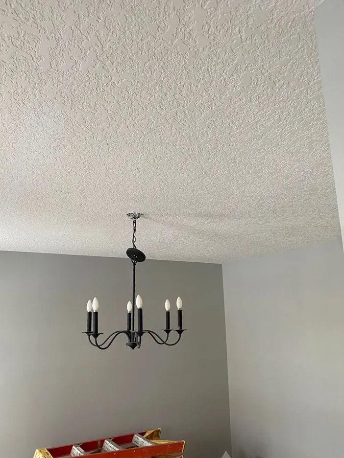 Black chandelier hanging from a textured white ceiling in a room with gray walls.