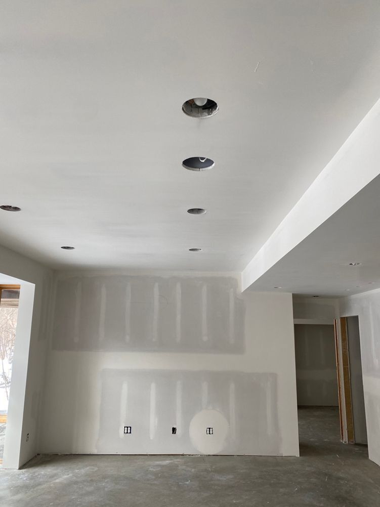 Interior view of a room under construction with recessed lighting in the ceiling and unfinished drywall.
