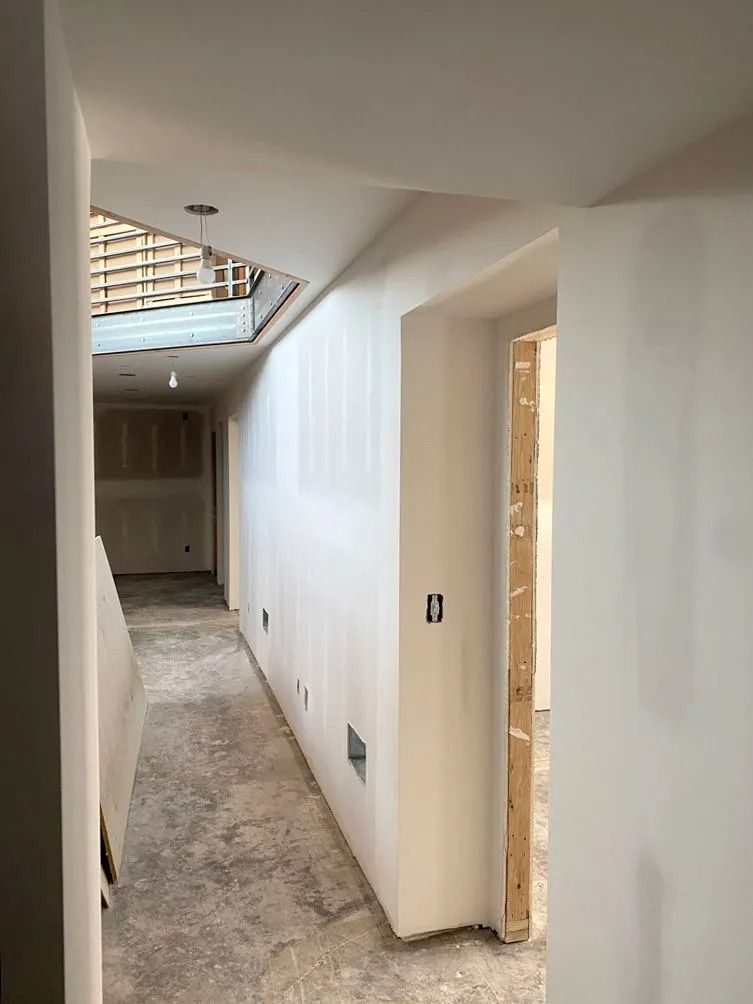 Interior hallway under construction, white walls, concrete floor, doorway on the right, skylight above.