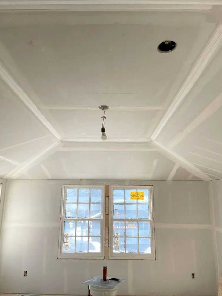 Interior view of a room under construction, featuring windows, a coffered ceiling, and exposed drywall.