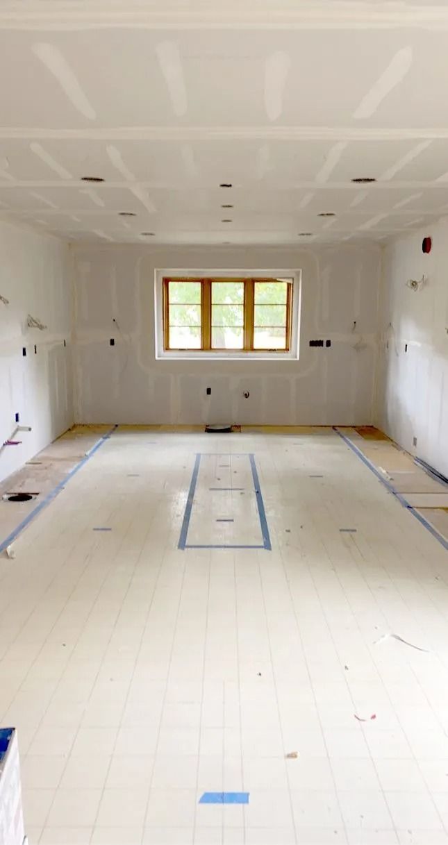 Interior room under construction, with drywall and electrical wiring exposed. Central window, unfinished floor.