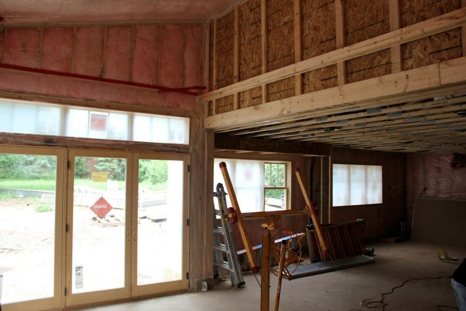 Interior view of a building under construction, showing wooden framing, insulation, and windows.