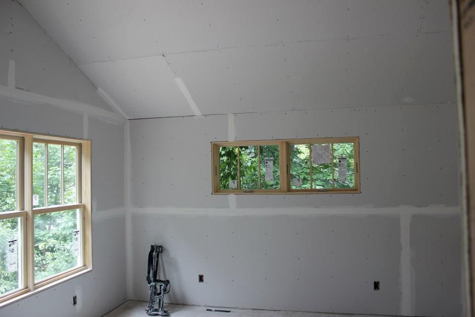 Interior of a room under construction with drywall and wooden window frames.