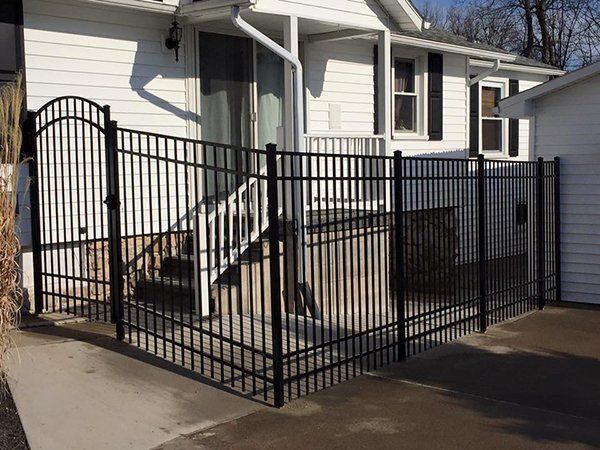 Black metal ramp and fenced porch beside a white house with steps and a garage.