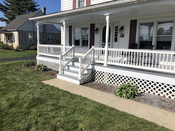 White house porch with railing, steps, and lattice skirting beside a green lawn