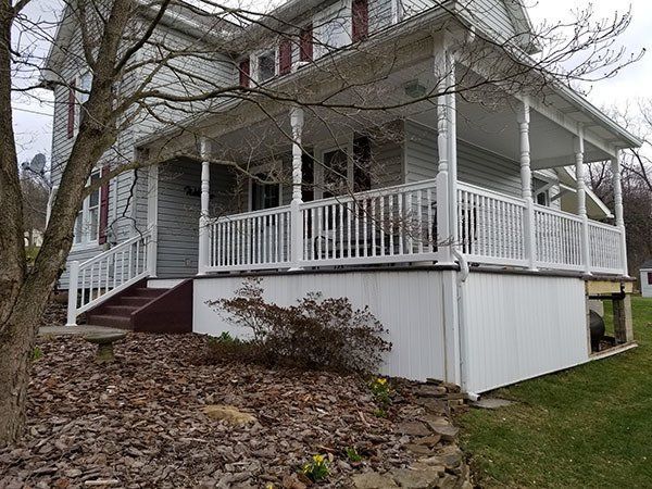 White house with a wraparound porch, white railing, and red steps on a sloped yard in winter