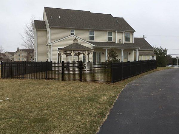 Two-story beige house with black fence and paved driveway on an overcast day