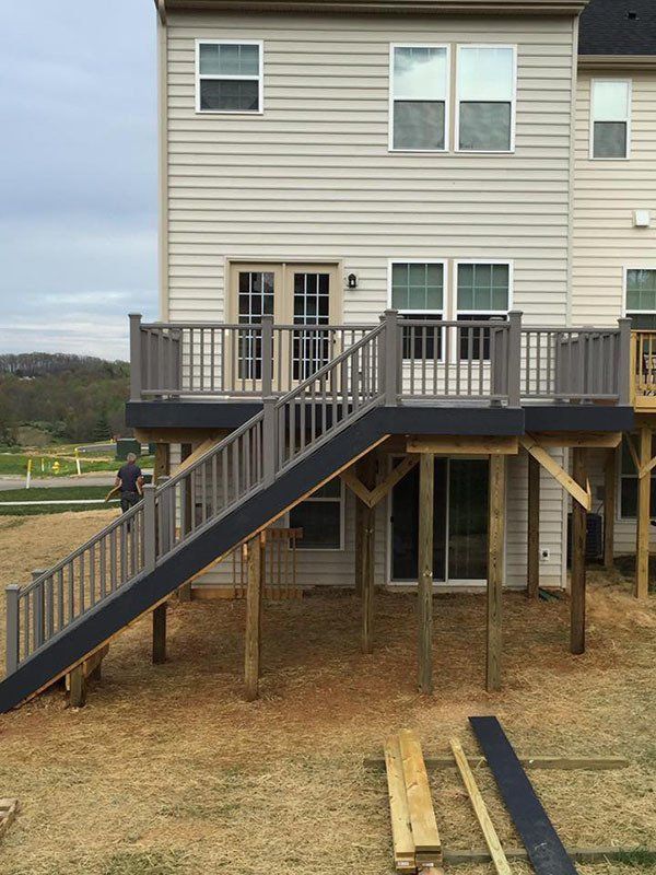 Raised house deck with dark stair ramp and railing, supported by posts over a dirt yard.
