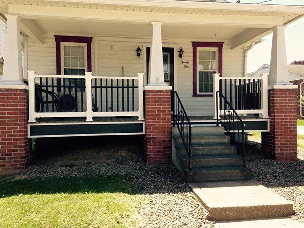 Front porch of a brick house with black railings and steps, viewed from the front lawn