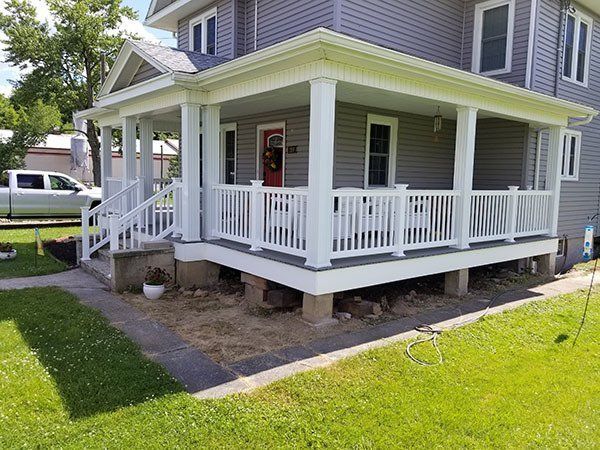 Gray house with white wraparound porch and railings on a sunny lawn