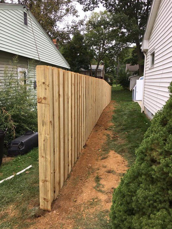 New wooden privacy fence along a narrow dirt path between two houses