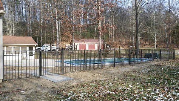 Fenced outdoor pool with blue railings beside small buildings and leafless trees in a wooded area