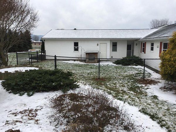 Snowy backyard with a white house, black fence, and bare trees