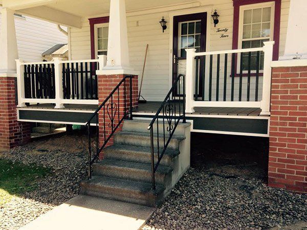 Front porch with brick steps, black railings, white columns, and a maroon front door on a house