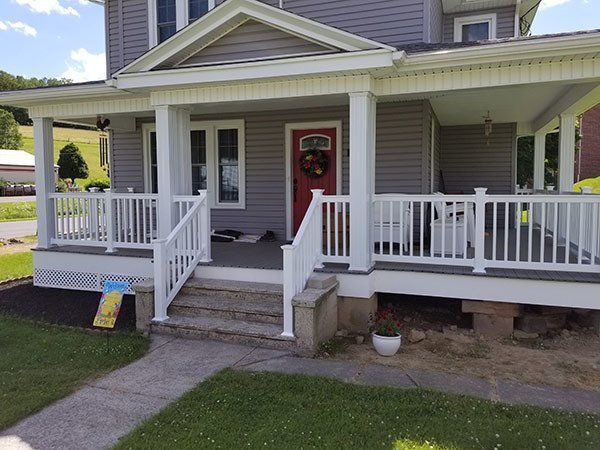 Front porch of a gray house with white railings and a red front door wreath