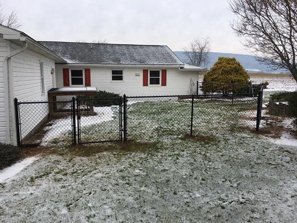 Snow-dusted yard with a white house, chain-link fence, and lake in the background