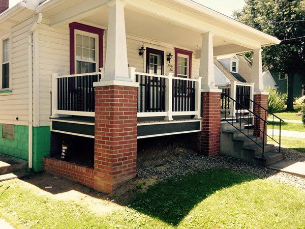Front porch of a beige house with white railings, red brick columns, and steps leading up from the yard