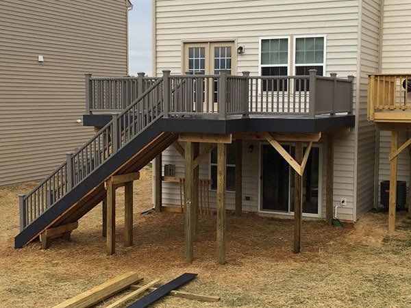 Elevated wooden deck with stairs and support posts beside a beige house in a yard