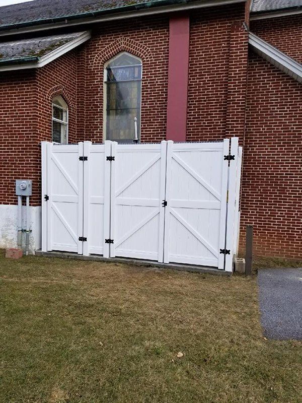White double gate in front of a red brick building with a small sign and grassy lawn