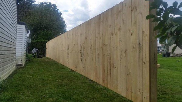 Long wooden privacy fence beside a grassy yard and house under a cloudy sky