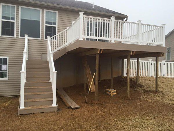 Back deck with stairs and white railing over a muddy yard, with construction materials underneath