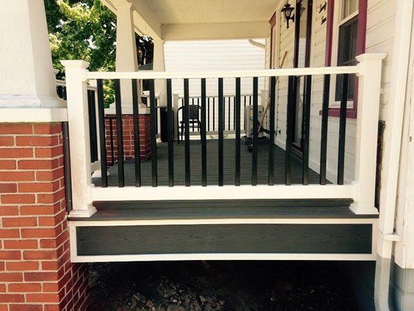 Front porch with white railing, black steps, and a red brick wall entrance