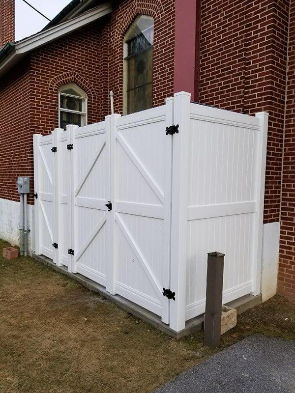 White wooden double gate beside a brick building, enclosing a small yard