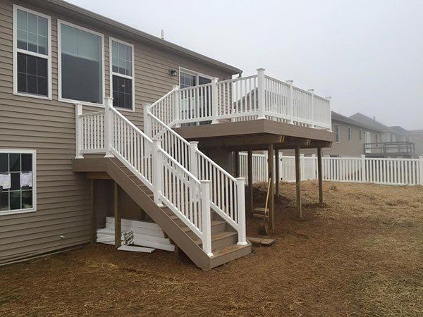 Raised backyard deck with white railing and stairs attached to a tan house.