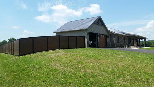 Barn and long dark fence beside a grassy field under a bright blue sky