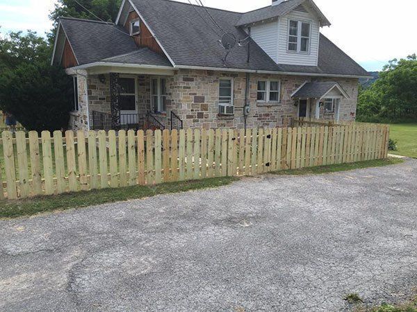Stone house with a light wooden fence beside a gravel driveway in a rural setting