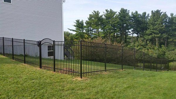 Black metal fence around a grassy backyard beside a white house, with trees in the background