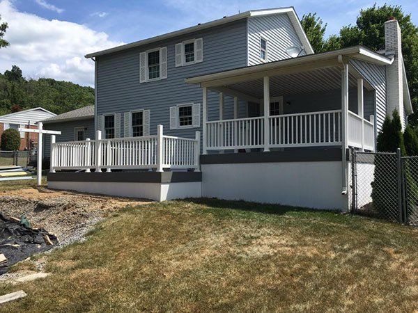 Gray two-story house with a wraparound porch on a grassy slope