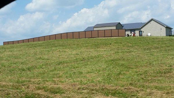 Grassy hill with a long brown fence and a house under a partly cloudy sky