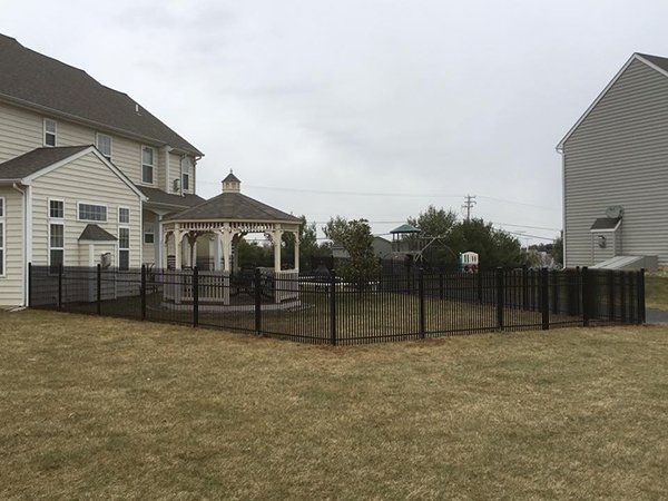 Suburban backyard with black metal fence, beige houses, and a small gazebo on a cloudy day