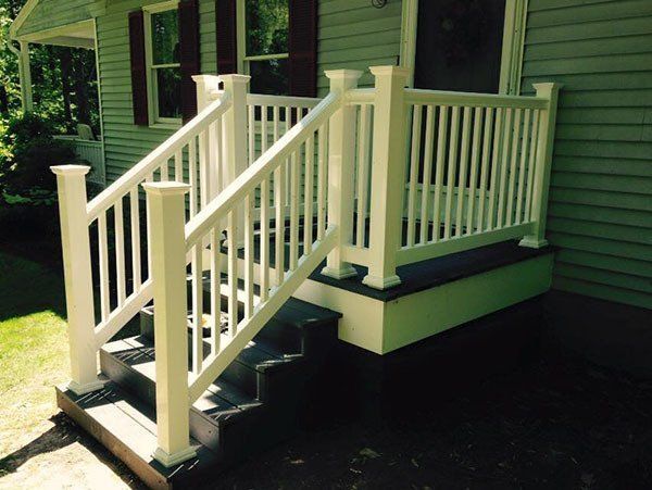 White porch ramp and steps with railings on a green house exterior.
