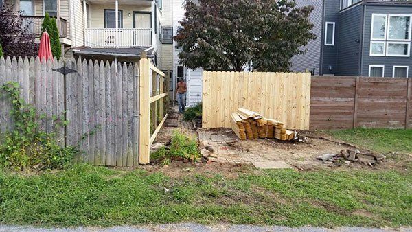 Backyard with a wooden fence, dirt clearing, and stacked lumber beside a grassy strip