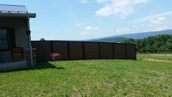 Grassy backyard beside a house with a dark fence and distant mountains under a clear sky