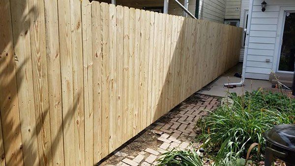 Wooden privacy fence along a narrow side yard beside a house and garden walkway.